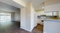 This single-floor residence offers a clean, functional layout with consistent dark hardwood-style flooring running throughout every room, creating a cohesive and polished aesthetic. Neutral warm-beige walls and white trim provide a bright, welcoming backdrop across the entire space.

The entry opens into a spacious living area featuring a textured ceiling and a sliding glass door that fills the room with natural light and provides direct access to the outdoors. A secondary living or dining area nearby includes a ceiling fan with a light fixture, adding comfort and airflow.

The kitchen is well-appointed with white cabinetry, light speckled countertops, a gas range, a full-size refrigerator, and an under-cabinet range hood. A double-basin sink sits beneath a window, and the layout provides ample counter and storage space for everyday use.

The bedrooms are generously proportioned, each featuring ceiling fans, natural light from windows with blinds, and neutral walls that lend a calm atmosphere. Closet access is present in multiple rooms.

The bathroom features a light speckled vanity countertop with built-in drawers, a large mirror, and a separate compartment housing a tub-shower combination and toilet. Additional storage closets are accessible from the hallway, contributing to the overall practicality of the floor plan.
