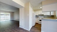 This single-floor residence offers a clean, functional layout with consistent dark hardwood-style flooring running throughout every room, creating a cohesive and polished aesthetic. Neutral warm-beige walls and white trim provide a bright, welcoming backdrop across the entire space.

The entry opens into a spacious living area featuring a textured ceiling and a sliding glass door that fills the room with natural light and provides direct access to the outdoors. A secondary living or dining area nearby includes a ceiling fan with a light fixture, adding comfort and airflow.

The kitchen is well-appointed with white cabinetry, light speckled countertops, a gas range, a full-size refrigerator, and an under-cabinet range hood. A double-basin sink sits beneath a window, and the layout provides ample counter and storage space for everyday use.

The bedrooms are generously proportioned, each featuring ceiling fans, natural light from windows with blinds, and neutral walls that lend a calm atmosphere. Closet access is present in multiple rooms.

The bathroom features a light speckled vanity countertop with built-in drawers, a large mirror, and a separate compartment housing a tub-shower combination and toilet. Additional storage closets are accessible from the hallway, contributing to the overall practicality of the floor plan.