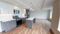 Unit 503 is a well-appointed 1-bedroom, 1-bathroom residence spread across a single floor. The open-concept layout seamlessly connects the kitchen, dining, and living areas, creating a spacious and functional flow throughout the unit.

The kitchen is a standout feature, outfitted with sleek two-tone cabinetry — combining white upper cabinets with dark wood-grain lower cabinets — and crisp white countertops. Stainless steel appliances include a gas range, built-in microwave, refrigerator, and dishwasher. A central kitchen island provides additional prep space and casual seating, while two elegant pendant lights hang above, adding a modern touch. Recessed lighting further brightens the space.

The living area is generously sized, benefiting from multiple windows that invite ample natural light. Warm hardwood-style flooring runs continuously throughout the main living spaces, contributing to a cohesive and inviting ambiance.

The bedroom offers a private retreat, and the bathroom is cleanly finished with contemporary fixtures. A tray ceiling detail in the main living area adds an architectural element that enhances the sense of height and refinement. The overall aesthetic is modern and clean, with a neutral palette that offers a versatile backdrop for any interior style.