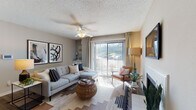 This single-story residence offers a well-organized layout with multiple rooms connected by a functional floor plan visible in the 3D overview. The living room serves as the central gathering space, featuring a white-tiled fireplace, ceiling fan, and a large sliding glass door that floods the room with natural light and provides views of the surrounding greenery. The open sightline from the living area extends into a dedicated dining space, which is illuminated by a pendant light and connects seamlessly to the rest of the home.

The galley-style kitchen is outfitted with white cabinetry, granite-look countertops, wood-look flooring, and black appliances including a range, refrigerator, and dishwasher, along with a gold-toned faucet at the sink. Two bedrooms provide comfortable retreats; one features carpeted flooring, a ceiling fan, and a window with outdoor views, while the other offers carpet, decorative wall art, and soft ambient lighting. Both bathrooms are functional and cleanly finished, each featuring a tub-shower combination—one with a granite-top vanity and wood-look flooring, the other with classic white tile surround. Textured ceilings are consistent throughout the residence.
