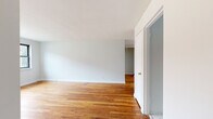 Located at 11 Centennial Dr in Syracuse, NY, this single-floor unit offers a straightforward and functional layout with a clean, understated aesthetic throughout. Rich hardwood flooring runs continuously through the main living areas and bedrooms, lending warmth and a sense of cohesion to the space. The open living area is generously proportioned, with white walls and smooth ceilings that create a bright, neutral canvas. Multiple rooms benefit from natural light streaming through black-framed windows, which frame views of the surrounding neighborhood greenery. Bedrooms are well-sized, with one featuring a built-in closet with a hanging rod for convenient storage, and radiator heating units are present throughout for comfortable warmth. The kitchen is equipped with a gas range, upper and lower cabinetry in a warm brown tone, a stainless steel sink with drainboard, and white tile backsplash. A window above the kitchen sink area brings in additional natural light. The bathroom includes a full soaking tub, white tile surround, and a window for ventilation. Light tile flooring completes the kitchen and bath areas. Overall, the unit presents a practical and livable space in a residential Syracuse neighborhood.