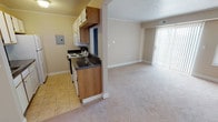 This single-floor residence offers a practical and comfortable layout designed for everyday living. The kitchen is efficiently arranged with wood-toned cabinetry, dark granite-style countertops, and a full suite of white appliances including a coil electric range, over-the-range microwave, refrigerator, and dishwasher. Light tile flooring runs throughout the kitchen, which opens directly into the living area for a seamless flow. The living room is generously sized, featuring neutral-toned carpet, crown molding, and a large sliding glass door dressed with vertical blinds that invites natural light and provides access to the outdoors. An additional window further brightens the space. The two bedrooms are comfortably proportioned, each finished with soft carpet and neutral wall tones. One bedroom features a ceiling fan with lighting, while both rooms include windows with blinds that allow for natural light and privacy. The bathroom is clean and functional, showcasing a full tub-and-shower combination with floor-to-ceiling subway-style tile, chrome fixtures, and built-in corner shelving. Crown molding and consistent neutral finishes throughout the space lend a cohesive and understated aesthetic from room to room.