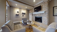 Located at 351 Peat Moss Dr in Columbus, OH, this single-story community clubhouse offers a thoughtfully designed amenity space with a variety of distinct areas for relaxation and recreation. The central great room commands attention with soaring ceilings and a dramatic floor-to-ceiling arched window arrangement that floods the space with natural light. Rich hardwood-style flooring anchors the open layout, which features a high-top communal table with cream upholstered seating — ideal for casual gatherings or work sessions.

The lounge area exudes warmth and comfort, centered around a striking floor-to-ceiling stacked stone fireplace topped with a mounted flat-screen television. Neutral-toned tufted sofas and accent chairs are arranged atop a colorful area rug, creating an inviting atmosphere. Crown molding and recessed lighting add refined architectural detail throughout.

A dedicated private theater room offers stadium-style seating with cushioned chairs equipped with cup holders, facing a large projection screen framed by rich draping curtains. Cinema-themed décor, including vintage film reel accents, enhances the immersive experience.

Additional amenities include a billiards table and a well-equipped fitness center visible through interior windows, rounding out this comprehensive and stylishly appointed community facility.