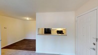 Located at 1749 Dobbins Dr in Chapel Hill, NC, this single-floor residence offers a practical and comfortable layout with a clean, neutral aesthetic throughout. The living area features warm hardwood-style flooring and connects seamlessly to the kitchen via a convenient pass-through window, enhancing the sense of openness between the spaces. The galley-style kitchen is well-appointed with white cabinetry, light countertops, dark hardwood-style flooring, and black appliances including a refrigerator, electric range, and dishwasher, with ample cabinet storage lining both sides of the space. The bedrooms are carpeted for comfort, each featuring natural light from windows with blinds. One bedroom includes a sliding glass door that opens to a private balcony with outdoor views, while another features a closet with a hanging rod for storage. The bathroom is straightforward and functional, equipped with a full bathtub, toilet, and dark hardwood-style flooring. Textured ceilings are present throughout the unit, and the overall color palette of warm beige and white tones lends the space a bright, neutral feel that adapts easily to a variety of furnishing styles.