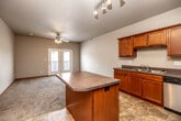 This single-floor space is designed with a functional, open layout that connects the kitchen and living areas seamlessly. The kitchen is well-appointed with warm-toned wooden cabinetry, dark laminate countertops, stainless steel appliances including a refrigerator, range, microwave, and dishwasher, and stone-look tile flooring. A central island with a curved countertop provides additional prep space and casual seating. The living area features plush carpeting, a ceiling fan with light fixture, and French doors that allow natural light to fill the space while offering access to the outdoors.

The unit includes multiple bedrooms, each finished with soft carpet, ceiling fans, and windows that bring in natural light. Closet space is provided in the primary bedroom. The primary bathroom features a dual-sink vanity with rich wooden cabinetry, a large mirror with vanity lighting, and stone-look tile flooring. A second full bathroom includes a soaking tub with shower, while an additional bathroom offers a standalone shower stall. Throughout, neutral wall tones and warm wood trim create a cohesive, comfortable atmosphere.