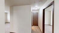 Located at 9118 E Columbia Dr in Spokane, WA, this one-bedroom, one-bathroom unit offers a practical and comfortable single-floor layout. The living room is bright and open, featuring plush wall-to-wall carpeting, neutral wall tones, and large windows fitted with blinds that allow natural light to fill the space. A sliding glass door provides outdoor access and additional light, while a wall-mounted HVAC unit ensures year-round climate control. The kitchen flows directly from the living area and is equipped with rich dark wood cabinetry extending to the ceiling for ample storage, a full suite of white appliances including a refrigerator and range, a double-basin sink with a dishwasher, and stone-patterned vinyl flooring. The bedroom is generously sized, featuring the same soft carpeting and a window with views of the surrounding neighborhood greenery. The full bathroom includes a dark wood vanity with a large mirror, a multi-bulb vanity light fixture, and neutral countertops. Dark wood trim and baseboards run consistently throughout the unit, adding a cohesive, polished contrast to the light walls and carpet. A dedicated utility room rounds out the functional layout of this well-appointed Spokane residence.