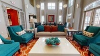 Located at 4660 Monroe Way in Fredericksburg, Virginia, this single-story community clubhouse by Breeden offers a well-appointed gathering and leasing facility designed with energy and style. The grand entrance greets visitors with soaring ceilings, arched transom windows, and large French doors that flood the space with natural light. Polished tile flooring anchors the welcoming lobby, which features elegant lounge seating and curated décor.

The main lounge area is a standout, boasting dramatic double-height ceilings, oversized windows dressed with floor-to-ceiling drapes, and a bold color palette of teal, orange, and cream. A marble-topped bar counter with pendant lighting and a built-in fireplace beneath a wall-mounted TV add to the space's sophisticated social atmosphere. Hardwood-style flooring runs throughout the lounge and connecting areas.

The leasing office features vibrant orange accent walls, contemporary workstations, and large-scale artwork, creating a professional yet inviting environment. A fully equipped kitchenette with granite countertops, white shaker cabinetry, and stainless steel appliances — including a refrigerator and dishwasher — provides functional amenity support. An additional full kitchen mirrors this design with matching cabinetry, a tile backsplash, and stainless steel appliances. Together, these spaces deliver a cohesive, community-focused experience.