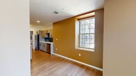 Located at 201 S Huntington Ave in Boston's Jamaica Plain neighborhood, this 2-bedroom, 2-bathroom unit offers a well-designed, single-floor layout. Warm hardwood-style flooring runs throughout, complemented by a color palette of earthy golden-amber and neutral tones that create an inviting ambiance.

The open-concept living, dining, and kitchen area is anchored by a galley-style kitchen featuring gray shaker cabinetry with matte black hardware, quartz countertops, a dark subway tile backsplash, and a full suite of stainless steel appliances. An in-unit stacked laundry is also conveniently included.

The living and dining area benefits from large grid-pane windows that bring in generous natural light and views of the surrounding Boston streetscape. Both bedrooms offer clean, bright interiors with the same hardwood-style flooring; the primary bedroom includes a double-door closet for ample storage.

The bathrooms are thoughtfully finished, with one featuring hexagonal floor tile, full subway tile surround, a soaking tub, and a window for natural ventilation. The unit's layout is efficient and functional, making excellent use of its compact footprint while maintaining a modern, cohesive aesthetic throughout.