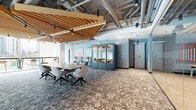 This thoughtfully designed single-floor commercial space offers a generous and versatile layout built for modern collaboration and productivity. Throughout the space, a distinctive signature element ties the design together: slatted wood ceiling baffles that add warmth and acoustic definition against exposed structural elements and industrial-style ductwork, creating a refined yet dynamic atmosphere.

The main open area features patterned carpet flooring, a central meeting table with ergonomic seating, and freestanding acoustic phone pods finished in muted blue-grey — ideal for private conversations. Colorful wall art adds a creative energy to the space, while floor-to-ceiling glazing along one edge floods the interior with natural light and offers views of the surrounding urban skyline.

A dedicated lounge zone features light wood wall paneling, a built-in linear fireplace, a wall-mounted display screen, and a built-in bench seat, providing a comfortable and inviting retreat. Adjacent to this is a recreation area with light hardwood flooring, a pool table, and casual seating.

The fully equipped kitchen is sleek and functional, boasting full-height cabinetry in a soft grey finish, stainless steel appliances including double wall ovens, under-cabinet lighting, and a large central island — all connected to an adjacent lounge nook bathed in natural light.