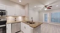This single-floor, one-bedroom unit offers a thoughtfully designed layout that maximizes its compact footprint. The open-concept living, dining, and kitchen area forms the heart of the space, finished with light wood-style flooring and neutral warm-gray walls that lend a clean, contemporary feel throughout.

The kitchen is well-equipped with a full suite of stainless steel appliances, including a refrigerator, range with over-the-range microwave, and dishwasher. White raised-panel cabinetry provides ample storage, while granite countertops with earthy tones add visual depth. A peninsula with a double stainless steel sink and a classic travertine tile backsplash rounds out the kitchen's polished aesthetic. Recessed lighting ensures the space is bright and functional.

The adjoining living area is finished with crown molding, recessed lighting, and a ceiling fan, contributing to a refined yet comfortable atmosphere. A glass-paneled door allows natural light to filter in, enhancing the sense of openness. The dining area features a large window with slatted blinds, offering additional natural light and outdoor views.

The bedroom is a comfortable, well-proportioned retreat with light wood-style flooring, neutral walls, and large windows that invite ample natural light. The overall design of the unit balances practicality with tasteful finishes, making it a welcoming and functional living space.