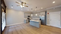 Located at 1230 Cottontown Rd in Forest, Virginia, this single-story home offers a thoughtfully designed open-concept layout that seamlessly connects the living and kitchen areas. Light-toned hardwood-style flooring flows throughout the main living space, complemented by crown molding and a ceiling fan that enhance the clean, contemporary aesthetic.

The kitchen is a standout feature, showcasing soft gray shaker-style cabinetry with brushed hardware, crisp white quartz countertops, and a classic subway tile backsplash in neutral tones. A central island with an integrated sink serves as both a functional workspace and a gathering point. Stainless steel appliances, including a range, over-the-range microwave, and a French door refrigerator with an ice and water dispenser, round out the well-equipped space. Pendant lighting with glass shades adds a refined touch above the island.

The dedicated laundry room is outfitted with a full-size top-loading washer and dryer, along with an overhead storage shelf for added convenience. The bathroom features a combined tub and shower unit with chrome fixtures and tile flooring, offering a clean and functional design. Throughout the home, recessed lighting and neutral wall tones create a bright, welcoming ambiance suited to a variety of interior styles.