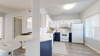 This thoughtfully laid-out 2-bedroom, 1-bathroom residence offers a cohesive and modern interior across a single floor. The kitchen is a standout feature, showcasing a striking two-tone design with crisp white upper cabinets and bold navy lower cabinets, accented by gold hardware. White quartz countertops and a peninsula with bar seating provide both style and functionality, while light wood-look flooring ties the space together seamlessly.

The open living room is bright and welcoming, filled with natural light from large windows and a sliding glass door that leads to an outdoor patio. Soft carpeting adds warmth underfoot, complementing the neutral, light gray walls throughout.

Both bedrooms are carpeted and offer a calm, restful atmosphere. The primary bedroom is comfortably sized, featuring a window that allows for natural light. A dedicated walk-in closet with built-in shelving provides ample storage.

The bathroom includes a shower-tub combination and shares space with an in-unit washer, adding everyday convenience. Light wood-look flooring continues into the bathroom, maintaining a consistent aesthetic. The overall design is clean, modern, and functional, making efficient use of every area within this well-appointed residence.