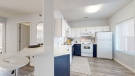 This thoughtfully laid-out 2-bedroom, 1-bathroom residence offers a cohesive and modern interior across a single floor. The kitchen is a standout feature, showcasing a striking two-tone design with crisp white upper cabinets and bold navy lower cabinets, accented by gold hardware. White quartz countertops and a peninsula with bar seating provide both style and functionality, while light wood-look flooring ties the space together seamlessly.

The open living room is bright and welcoming, filled with natural light from large windows and a sliding glass door that leads to an outdoor patio. Soft carpeting adds warmth underfoot, complementing the neutral, light gray walls throughout.

Both bedrooms are carpeted and offer a calm, restful atmosphere. The primary bedroom is comfortably sized, featuring a window that allows for natural light. A dedicated walk-in closet with built-in shelving provides ample storage.

The bathroom includes a shower-tub combination and shares space with an in-unit washer, adding everyday convenience. Light wood-look flooring continues into the bathroom, maintaining a consistent aesthetic. The overall design is clean, modern, and functional, making efficient use of every area within this well-appointed residence.