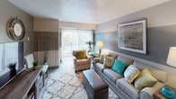 Located at 11580 Somerset Dr in North Royalton, Ohio, this well-appointed single-floor residence offers a thoughtfully designed layout that balances comfort and functionality. The living room serves as the heart of the home, featuring a two-tone accent wall in soft gray and blue hues, textured ceilings, and large sliding glass doors that flood the space with natural light and provide direct access to an outdoor patio area. The galley-style kitchen is efficiently organized with white cabinetry, dark granite-style countertops, tile flooring, and black appliances including a range, refrigerator, and dishwasher, all beneath a skylight-style ceiling panel. Adjacent to the kitchen is a cozy dining nook, ideal for intimate meals. The primary bedroom is generously sized with plush carpeting, natural light from a large window, and ample closet space featuring full-width sliding doors. A second bedroom offers similar carpeted comfort, a sizable window with outdoor views, and room for a dedicated workspace. The full bathroom includes a tub-shower combination with tiled surround, tile flooring, and overhead cabinetry for storage. Throughout the residence, neutral tones and soft finishes create a warm, inviting ambiance.