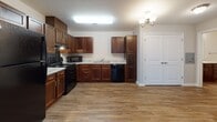 Located at 5002 Strauss Ct in Fredericksburg, Virginia, this single-floor unit offers a practical and well-appointed layout with consistent finishes throughout. The kitchen is a standout feature, showcasing rich dark-stained cabinetry in an L-shaped configuration paired with light granite countertops. Black appliances — including a refrigerator, electric range, microwave, and dishwasher — complement the cabinetry, while wood-look plank flooring ties the space together. A double-basin sink sits beneath overhead cabinets, maximizing storage and functionality.

The open area adjacent to the kitchen provides versatile living space, illuminated by a classic chandelier and featuring a set of double doors for added storage. The bedrooms are carpeted and each include ceiling fans with lighting, offering comfort year-round. Windows in each bedroom allow natural light and neighborhood views.

Two bathrooms serve the unit — one featuring a full tub-shower combination with chrome fixtures, and a second with grab bars and a granite-topped vanity, both finished with wood-look flooring. Neutral wall tones and clean white trim carry throughout, creating a cohesive and move-in-ready environment.
