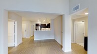 Located in San Diego's Carmel Creek area, this single-story residence showcases a thoughtfully designed open-concept layout that seamlessly connects the living and kitchen areas. The space features warm wood-style flooring throughout, contributing to a cohesive and contemporary aesthetic.

The kitchen is a standout feature, equipped with dark espresso cabinetry, a mosaic tile backsplash, stainless steel appliances, and a peninsula with a white countertop that doubles as a breakfast bar. Pendant lighting hangs above the peninsula, adding both functional illumination and a modern design touch. Recessed lighting throughout the kitchen ensures the space is well-lit.

The open living area benefits from high ceilings that enhance the sense of spaciousness, while neutral-toned walls create a clean, versatile backdrop. A hallway visible from the main living space leads to additional rooms, each accessible through clean white doors that complement the overall light and modern interior palette. The layout promotes an easy flow between spaces, making the residence feel open and functional throughout.