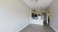 Located at 3 Sundial in Manchester, New Hampshire, this single-floor residence offers a thoughtfully designed open-concept living space that feels airy and expansive. The soaring vaulted ceilings draw the eye upward, amplifying the sense of openness throughout the main living area, which is finished with smooth neutral-toned walls and durable wood-look plank flooring in a warm gray hue.

The kitchen serves as a central focal point, seamlessly integrated into the living space. It features dark cabinetry paired with light countertops, creating a striking contrast that adds visual depth. A peninsula with a built-in sink offers additional prep space and a natural gathering point. Pendant lighting hangs above the peninsula, providing both task illumination and a modern decorative element. A stainless steel refrigerator and stainless range hood complete the contemporary kitchen aesthetic.

A ceiling fan in the living area ensures year-round comfort, while recessed and track lighting throughout provide versatile ambient and accent illumination. Clean white baseboards and crisp door trim lend a polished, finished look to each corner of the space. The overall ambiance is modern and minimalist, offering a clean, move-in-ready environment well-suited for comfortable everyday living.