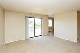 This single-floor residence offers a practical and comfortable layout with a consistent neutral color palette, textured ceilings, and wall-to-wall carpeting throughout the living and bedroom areas. The kitchen is well-equipped with warm wood-tone cabinetry offering generous storage, light countertops, a double-basin sink, and white appliances including a refrigerator, dishwasher, and range. The flooring in the kitchen features durable tile in an earthy tone, providing a functional contrast to the carpeted rooms. The bedrooms are spacious and bright, each featuring large windows that invite natural light and offer views of surrounding greenery. The rooms provide ample wall space and are finished with clean white baseboards against the warm taupe walls. The living area is a highlight of the space, featuring a sliding glass door that opens to a private balcony overlooking a lush, tree-lined outdoor setting — ideal for enjoying natural surroundings. Two bathrooms serve the space, both featuring light wood vanity cabinetry, round undermount sinks with light countertops, well-lit mirrors, and warm-toned wood upper cabinets for additional storage. The overall ambiance of the space is clean, neutral, and move-in ready, offering a functional and inviting environment.