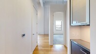 Located on the 10th floor at 215 W Pershing Rd in Kansas City, MO, this one-bedroom, one-bathroom unit offers an open and airy layout with industrial-inspired design elements. The main living area features warm hardwood flooring, soaring exposed ceilings with visible structural beams and ductwork, and a pendant light fixture that adds character to the space. A kitchen counter with a dark stone surface is partially visible, seamlessly integrating with the open-plan living area.

The bedroom is carpeted in a neutral blue-gray tone and benefits from generous natural light through a large window framing city skyline views. Exposed ductwork along the upper walls continues the unit's industrial aesthetic into this private retreat.

The bathroom is clean and modern, featuring large-format white floor tiles, full white subway tile walls, and a glass-enclosed walk-in shower. A dark wood vanity with a white countertop provides a refined contrast to the bright, minimalist surroundings.

Throughout the unit, tall ceilings and crisp white walls create a sense of openness well beyond the unit's compact footprint. The combination of industrial character and contemporary finishes makes this a distinctive urban residence in the heart of Kansas City.