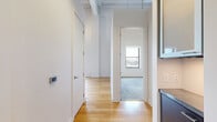 Located on the 10th floor at 215 W Pershing Rd in Kansas City, MO, this one-bedroom, one-bathroom unit offers an open and airy layout with industrial-inspired design elements. The main living area features warm hardwood flooring, soaring exposed ceilings with visible structural beams and ductwork, and a pendant light fixture that adds character to the space. A kitchen counter with a dark stone surface is partially visible, seamlessly integrating with the open-plan living area.

The bedroom is carpeted in a neutral blue-gray tone and benefits from generous natural light through a large window framing city skyline views. Exposed ductwork along the upper walls continues the unit's industrial aesthetic into this private retreat.

The bathroom is clean and modern, featuring large-format white floor tiles, full white subway tile walls, and a glass-enclosed walk-in shower. A dark wood vanity with a white countertop provides a refined contrast to the bright, minimalist surroundings.

Throughout the unit, tall ceilings and crisp white walls create a sense of openness well beyond the unit's compact footprint. The combination of industrial character and contemporary finishes makes this a distinctive urban residence in the heart of Kansas City.
