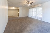 This single-story unit in Midland, Texas, offers a practical and functional layout across several well-defined spaces. The living area serves as the heart of the home, featuring wall-to-wall carpet in a warm neutral tone, a textured ceiling, and a ceiling fan with integrated lighting. Large sliding glass doors flood the room with natural light and provide outdoor views, complemented by an additional window fitted with horizontal blinds. The open sightline to the kitchen enhances the sense of connectivity throughout the main living space.

The galley-style kitchen is efficiently designed with warm wood cabinetry lining both sides, white countertops, and wood-look flooring. Stainless steel appliances, including a refrigerator, electric range, built-in microwave, and dishwasher, are neatly integrated. A skylight-style overhead fixture brightens the space, and a doorway at the end provides access to additional areas of the unit.

The bedrooms are carpeted and finished with neutral walls and textured ceilings. One bedroom includes two closets and a window, offering ample storage and natural light. Additional bedrooms feature windows with blinds. The bathroom includes a full tub-shower combination, a toilet, and wood-look flooring, presented in a clean, straightforward layout.