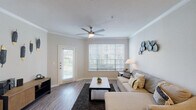 This single-story, one-bedroom, one-bathroom residence offers a thoughtfully designed layout that maximizes both functionality and comfort. Wood-style flooring flows throughout the unit, creating a cohesive aesthetic that ties each space together.

The living room serves as the heart of the home, featuring crown molding, a ceiling fan, and large windows that invite generous natural light. A private exterior door provides convenient outdoor access, enhancing the sense of openness in this welcoming space.

The kitchen is equipped with stainless steel appliances, including a refrigerator, electric range, and over-the-range microwave. White cabinetry pairs with granite-style countertops, and a peninsula counter provides additional workspace and a casual dining option. A walk-in pantry or storage closet offers practical organization space.

The bedroom is a calm, well-sized retreat featuring a ceiling fan, a window for natural light, and direct access to a spacious walk-in closet. The full bathroom includes a tub-shower combination with a tile surround, wood-style flooring, a large vanity mirror, and a single-sink vanity, all presented in a clean, neutral palette.