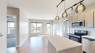 Located on South Grand Boulevard in St. Louis, Missouri, this single-floor residence offers a sleek, contemporary design throughout. The open-concept living and kitchen area is anchored by warm hardwood-style flooring and flooded with natural light through large windows and a glass door that leads to a private balcony, offering pleasant outdoor views of the surrounding neighborhood.

The kitchen is a standout feature, equipped with stainless steel appliances including a French door refrigerator, range, microwave, and dishwasher. Light wood-tone cabinetry, a white penny-tile backsplash, and crisp quartz countertops lend the space a clean, modern aesthetic. A central island provides additional prep and seating space, while stylish pendant lights hang overhead from a track lighting system that extends into the living area.

The bedrooms are carpeted for comfort, each offering ceiling fans and generous closet space, including a walk-in closet with built-in shelving. The unit also includes a well-appointed bathroom with modern fixtures, a rectangular undermount sink, and quartz countertops. A dedicated laundry area and smart home thermostat add further convenience. The overall palette of soft grays and warm neutrals creates a calm, inviting ambiance throughout.