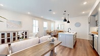This two-story home in San Antonio, TX offers a thoughtfully designed layout spread across two well-proportioned floors. The main level features an open-concept living, dining, and kitchen area bathed in natural light from multiple windows with white plantation shutters. Warm hardwood-style flooring runs throughout, complementing the neutral, bright color palette. The kitchen is a standout, boasting gray shaker cabinets, white quartz countertops, a subway tile backsplash, stainless steel appliances, and a center island with bar seating beneath stylish matte black pendant lights. The dining area accommodates a full-size table and opens directly to an outdoor patio, while the living room offers a comfortable, airy retreat. Three well-appointed bathrooms are distributed across the home, featuring white cabinetry with quartz counters, dark fixtures, tile flooring, and a glass-enclosed walk-in shower in one. Upstairs, two carpeted bedrooms are filled with natural light from dual windows, each offering a calm and restful atmosphere with dedicated closet space. A hallway and two staircases connect the floors efficiently. The home's clean, contemporary aesthetic is consistent throughout, making it a well-organized and inviting space.