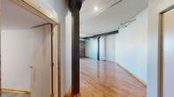Located in the heart of downtown Davenport, Iowa, this urban loft blends historic industrial character with modern finishes across a single, generously sized floor. Original exposed brick walls, bold steel support columns, and visible ductwork pay homage to the building's industrial past, while warm hardwood floors throughout create an inviting contrast. The open living area is expansive and light-filled, with large arched windows offering views of the surrounding cityscape. Track lighting and a ceiling fan add functional style to the space. The modern kitchen is a standout feature, equipped with stainless steel appliances—including a gas range, microwave, dishwasher, and French door refrigerator—white shaker cabinetry, a granite-topped island, and pendant lighting, all set against soaring ceilings. A stacked washer and dryer unit is conveniently integrated nearby. The spacious primary bedroom features exposed brick, hardwood floors, and a bright window. Both bathrooms are clean and contemporary, with white vanities, tile flooring, and a walk-in shower. This loft delivers an authentic urban living experience in a character-rich building in the heart of the Quad Cities.