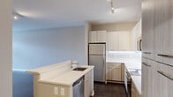 Located at 3300 Ann Arbor Saline Rd in Ann Arbor, MI, this well-appointed one-bedroom, one-bathroom unit offers a thoughtfully designed single-floor layout with modern finishes throughout. The open-concept kitchen and living area serves as the heart of the home, featuring a peninsula with quartz countertops and an undermount sink, two-tone cabinetry in white and warm wood tones, stainless steel appliances including a refrigerator, stove, built-in microwave, and dishwasher. Dark hardwood-style flooring flows throughout the main living areas, adding warmth and contrast to the neutral color palette. The living room receives natural light through a large window, creating a bright and inviting atmosphere. The bedroom is a comfortable retreat finished with plush carpeting, a generous window with outdoor views, and access to a spacious walk-in closet outfitted with wire shelving. The bathroom features a white vanity with ample drawer storage, a large mirror, and a shower-tub combination with wood-look flooring. A dedicated laundry room houses a full-size washer and dryer alongside a water heater, adding everyday convenience. Clean lines, neutral tones, and quality finishes give this unit a contemporary and functional character throughout.