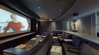 This refined single-floor screening and meeting facility is thoughtfully designed to deliver an immersive, upscale experience. The centerpiece is a dedicated home theater room appointed with tiered seating, featuring plush, curved black leather recliners and stylish patterned ottomans arranged for optimal sightlines to a large projection screen. Recessed ceiling lighting, a coffered circular ceiling detail, and floor-to-ceiling charcoal drapery panels create a dramatic, light-controlled atmosphere ideally suited for cinematic viewing. A ceiling-mounted projector and warm accent lighting along the side walls complete the professional setup.

Adjacent to the theater is a versatile presentation or conference room, equipped with a long, sleek white curved table surrounded by upholstered rolling chairs. A wall-mounted display screen makes this space well-suited for screenings, presentations, or collaborative meetings. Framed contemporary artwork adds a curated, sophisticated touch throughout.

A dedicated refreshment station connects the spaces, featuring dark cabinetry beneath a bright white countertop set against a striking herringbone-patterned tile backsplash. Decorative vessels and glassware are neatly arranged, reinforcing the polished, hospitality-forward character of the entire facility.