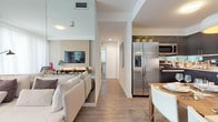 This well-designed single-floor residence offers a seamless blend of modern style and functional living. The open-concept layout connects the living, dining, and kitchen areas, creating a cohesive and welcoming environment. The living room features wood-look flooring, a textured accent wall with a wall-mounted television and a built-in floating media shelf with warm underlighting, and a large sectional sofa. A floor-to-ceiling mirror panel amplifies the sense of space and light in the room.

The kitchen is outfitted with dark espresso cabinetry, granite countertops, a mirrored backsplash, and a full suite of stainless steel appliances including a French door refrigerator, range, microwave, and dishwasher. A dining area with a pendant light fixture sits adjacent to the kitchen, ideal for entertaining.

The primary bedroom is a serene retreat with warm neutral tones, multiple windows with plantation shutters, a mirrored accent wall, a dedicated vanity area, and an en-suite bathroom. The second bedroom is equally comfortable, featuring natural light and a calm, neutral palette. The bathrooms are finished with large-format tile surrounding a soaking tub and shower combination. Wood-look flooring flows throughout the main living areas, tying the space together cohesively.