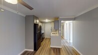 This single-floor residence showcases a thoughtfully designed open-concept layout finished with warm wood-look luxury vinyl plank flooring throughout. The entryway opens into a bright, airy living area accented by crown molding, recessed lighting, and a ceiling fan, with a large sliding glass door that floods the space with natural light and provides access to the outdoors.

The kitchen is well-equipped with gray shaker-style cabinetry, light quartz countertops, and a suite of black stainless steel appliances including a refrigerator, electric range, and microwave. A peninsula with a built-in sink offers additional prep space and a natural transition into the open living and dining areas.

The bedrooms are generously sized, each featuring ceiling fans, natural light from window blinds, and neutral gray walls. One bedroom includes a built-in closet with sliding doors, providing ample storage. A hallway connects the private areas of the residence, which includes a clean, modern bathroom outfitted with gray vanity cabinetry, a white quartz countertop, a tub-shower combination with glass sliding doors, and light tile flooring. The consistent use of neutral tones and updated finishes throughout creates a cohesive and inviting atmosphere.