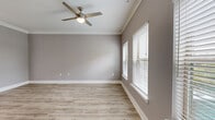 This thoughtfully designed one-bedroom, one-bathroom unit offers a cohesive and modern living experience across a single floor. Light wood-style flooring, neutral gray walls, crisp white crown molding, and white baseboards run consistently throughout, creating a clean, unified aesthetic.

The combined kitchen and living area serves as the heart of the unit. The kitchen is equipped with dark espresso cabinetry, stainless steel appliances — including a refrigerator, microwave, and range — granite countertops, a peninsula with a built-in sink, and pendant lighting overhead. A track light fixture adds further illumination to the space.

The living area is open and airy, benefiting from multiple windows with white horizontal blinds that allow generous natural light to fill the room. A stylish ceiling fan with a built-in light fixture is centrally mounted. The entry door, finished in a coordinating gray panel style, opens directly into this welcoming space.

The bedroom is comfortably sized, featuring a ceiling fan, a window with outdoor views of greenery, and direct access to both the closet and the bathroom. The bathroom is well-finished, offering a dark vanity with granite countertops, a framed mirror, and a tub-shower combination with white tile surround.