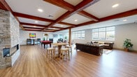 Located at 50 Bridge St in Shelton, Connecticut, this generously sized amenity space offers a thoughtfully designed single-floor layout that blends industrial character with modern comfort. The open living area is immediately striking, defined by rich, dark-stained exposed wood ceiling beams that lend warmth and architectural depth to the space. Wide-plank hardwood-style flooring flows throughout, anchoring the various activity zones with a cohesive, inviting feel.

A dramatic floor-to-ceiling stone fireplace serves as the centerpiece of the lounge, providing a natural focal point that separates the open gathering areas. Large, grid-pane windows line the exterior walls, bathing the space in natural light and offering views of the surrounding Shelton streetscape. The living area accommodates multiple seating arrangements, including tufted leather sofas and club chairs, alongside a bar-height pub table.

The game room features a regulation pool table and a dedicated poker room with a custom round gaming table, decorative pendant lighting, and a view of the historic downtown. The office area provides built-in workstations with computers and a printer, set against a wall of windows. A fully tiled, ADA-accessible bathroom completes the floor plan, ensuring functionality and inclusivity throughout the space.