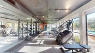 This fitness center is designed to accommodate a comprehensive range of workout needs within a single-story layout. The main exercise area is an elongated, open space with a textured exposed ceiling finished in a dark, industrial tone, complemented by track and pendant lighting that adds warmth throughout the room. Large windows line the perimeter walls, allowing generous natural light to pour in while offering outdoor views of surrounding greenery.

The cardio zone features Matrix-brand stair climbers, ellipticals, and treadmills arranged along the windowed walls. Opposite these machines, a row of power racks with barbells and a full dumbbell rack serves the strength training area, with floor-to-ceiling mirrors amplifying the sense of space. A cable machine station provides additional functional training options.

A bold, curved orange and white mural serves as a striking focal point on the rear accent wall, adding a vibrant, modern aesthetic to the space. Rubber flooring throughout the main area ensures durability and safety during workouts.

Adjacent to the main floor is a separate studio room featuring light hardwood flooring, a ceiling fan, full mirrored wall, and direct access to an outdoor pool area, making it well-suited for yoga, stretching, or group fitness classes.