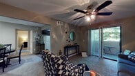 Located at 301 Dover Glen Drive in Nashville, Tennessee, this single-floor residence offers a well-organized layout with distinct living, dining, kitchen, bedroom, and bathroom areas. The living room is finished with plush carpeting and features a ceiling fan with light fixture, neutral taupe walls, and a sliding glass door fitted with vertical blinds that opens directly onto a private balcony with outdoor seating — allowing natural light and greenery views to filter into the space. The kitchen is equipped with dark espresso cabinetry, granite-style countertops, white appliances including a range and refrigerator, and wood-look vinyl flooring, with a window above the counter providing additional natural light. The bedroom is generously sized with soft carpet, a large window overlooking lush greenery, and a reach-in closet offering ample storage. The bathroom features dark cabinetry with a granite-style vanity top, a large mirror with overhead lighting, and wood-look flooring that complements the kitchen finishes. The dining area is a defined nook with carpeted flooring, a pendant light fixture, and wall-mounted shelving, creating an intimate space for meals. Throughout the residence, a cohesive neutral color palette and consistent dark cabinetry accents create a unified, modern aesthetic.
