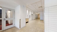 The lobby at 2060 Quingate Place in Halifax, Nova Scotia offers a well-appointed and functional entry experience across a single floor. The space is laid out across three interconnected hallway sections that together form an L-shaped corridor, providing clear circulation paths throughout the building's common areas.

The interior is defined by crisp white walls, a drop ceiling with recessed pot lighting, and large-format terrazzo tile flooring that lends a durable yet refined aesthetic throughout. White ceramic tile wainscoting adds architectural detail in key areas, complementing the clean, contemporary palette.

A prominent mailroom area features an extensive bank of individual mailboxes set into a tiled surround, serving the building's residents efficiently. Nearby, a small built-in cabinetry unit provides a convenient surface for parcel handling or correspondence. Multiple elevator bays are accessible directly from the main corridor, with pendant lighting and mirrored accents enhancing the sense of depth and brightness.

The lobby also provides access to additional building amenities, including a fitness facility visible through glazed doors, as well as stairwell access. Security features including an intercom entry system and surveillance cameras are integrated throughout. The overall ambiance is bright, functional, and well-maintained, reflecting a professionally managed residential building designed to facilitate ease of movement and resident convenience.