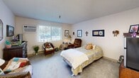 Located at 606 E Best Ave in Coeur d'Alene, Idaho, this single-floor studio-style unit offers an efficient and functional layout that combines living and sleeping spaces within one cohesive room. The bedroom area features soft wall-to-wall carpeting, neutral-toned walls, and a textured ceiling, creating a calm and comfortable atmosphere. A large sliding window allows natural light to fill the space while offering views of the surrounding greenery. A wall-mounted HVAC unit provides climate control year-round. Transitioning toward the kitchenette, the flooring shifts to light hardwood-style planks, adding visual distinction between the two functional zones. The kitchenette is equipped with warm-toned wood cabinetry, a compact stainless steel refrigerator, microwave, and a sink, making it practical for everyday use. A skylight overhead bathes the kitchen area in additional natural light. The overall layout is thoughtfully designed to maximize every square foot, with ample wall space for décor and personal touches. Neutral finishes throughout give the space a clean, adaptable canvas. This unit is well-suited for those seeking a manageable, self-contained living space in the heart of Coeur d'Alene.