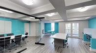 This single-floor workspace offers a thoughtfully designed environment that balances open collaboration with private workspaces. The interior is defined by a striking combination of crisp white walls and bold teal accent walls, creating a vibrant yet professional atmosphere. Hardwood-style flooring runs throughout, adding warmth and continuity across the space.

A standout feature is the glass partition system, which divides the space into distinct work zones while maintaining visual connectivity and an open feel. The glass-walled office area is outfitted with sleek black-framed ergonomic chairs and white desks, providing a clean, modern aesthetic. An adjacent open area features a round table with teal chairs, ideal for small group meetings or collaborative sessions.

The ceiling incorporates a layered, coffered design with recessed sections painted in contrasting gray, adding architectural depth and visual interest. Flush-mount lighting fixtures provide consistent, even illumination throughout. French doors at the rear of the space open to a balcony, allowing natural light to filter in and offering a refreshing outdoor view. Overall, the space is well-suited for a professional office or coworking environment.