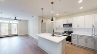 Located at 400 Universal Rd in Southern Pines, NC, this well-appointed 3-bedroom, 2-bathroom residence offers a thoughtfully designed single-floor layout. The open-concept kitchen and living area serves as the heart of the home, featuring a central island with pendant lighting, crisp white shaker cabinetry with matte black hardware, white quartz countertops, and stainless steel appliances including a range, microwave, and refrigerator. Warm hardwood-style flooring flows consistently throughout the entire space, creating a cohesive and inviting atmosphere.

The generously sized primary bedroom provides ample space and connects to the hallway, while two additional bedrooms each offer ceiling fans, natural light from windows with blinds, and access to closets. One bedroom features French doors opening to an outdoor balcony, adding a bright and airy feel. Four closets in total provide excellent storage throughout the unit.

Both bathrooms are finished with gray shaker-style vanities and white quartz countertops with matte black accents. The primary bath includes a dual-sink vanity with modern sconce lighting and a large mirror, while the secondary bath features a single vanity with a window for natural light. Clean white walls and consistent finishes lend a modern, move-in-ready aesthetic throughout.