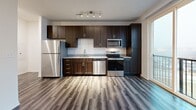 Located at 31 Sunnen Drive in Maplewood, Missouri, Unit 2-305 is a thoughtfully designed studio residence that maximizes its efficient footprint with modern finishes and an open layout. Rich, wood-look vinyl plank flooring extends throughout the entire unit, providing a warm and cohesive aesthetic from entry to balcony.

The kitchen is a standout feature, outfitted with a full suite of stainless steel appliances including a refrigerator, range, microwave, and dishwasher. Dark espresso-toned cabinetry reaches to the ceiling, offering generous storage, while granite countertops add a refined touch. Track lighting above illuminates the workspace effectively.

The open living area flows directly from the kitchen toward a sliding glass door that leads to a private balcony, allowing natural light to fill the space and providing views of the surrounding area. The main living space is clean and versatile, with neutral walls and recessed lighting.

The bathroom is neatly appointed with the same wood-look flooring, a tub-shower combination with clean white surrounds, a toilet, and a tall dark-wood storage cabinet with brushed nickel hardware, complementing the unit's consistent design language.

Overall, the unit presents a contemporary, move-in-ready interior with a cohesive palette of dark wood tones, stainless steel, and neutral walls.