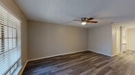 Located at 4412 Glenview Ct in North Richland Hills, TX, this single-story home offers a well-organized layout with a variety of thoughtfully finished spaces. The main living area is among the most prominent features of the home, showcasing rich, dark hardwood-style flooring that runs throughout much of the space. A textured ceiling and a five-blade ceiling fan with integrated lighting add both character and practicality to this generously sized room.

The kitchen is notably updated, featuring crisp white cabinetry with brushed nickel hardware, light quartz-style countertops, a classic white subway tile backsplash, a stainless steel sink, and a black electric range with overhead ventilation. Light wood-tone flooring ties the kitchen's clean aesthetic together.

The bedrooms offer a mix of flooring options, with some rooms featuring lighter hardwood-style planks and others finished with plush carpet, providing comfort underfoot. Several bedrooms are equipped with ceiling fans and windows fitted with horizontal blinds, allowing for natural light and outdoor views while maintaining privacy.

The bathroom presents a clean, functional design with white cabinetry, a tiled shower-tub combination, and matching light wood-tone flooring consistent with other areas of the home. Neutral wall tones throughout the property create a cohesive, move-in-ready atmosphere.
