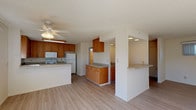 This two-story home is designed with a practical, open layout that promotes a bright and functional living environment. The main level centers around a spacious open-concept living and kitchen area, where light wood-style laminate flooring flows throughout. A ceiling fan overhead provides comfort, while natural light pours in through well-placed windows. The kitchen is well-appointed with warm-toned wood cabinetry, light countertops offering ample workspace, and white appliances including a range, over-the-range microwave, and refrigerator. A peninsula with a breakfast bar adds additional counter space and defines the transition between the kitchen and living area. A staircase with a decorative iron railing connects the main level to the upper floor. The bedrooms feature the same wood-style flooring, windows for natural light, and sliding or standard closets providing useful storage. The bathrooms are finished in a clean, neutral palette, each featuring wood-toned vanities, white countertops, and light flooring. One bathroom includes a tub-shower combination with a glass sliding door, while another features a standalone walk-in shower. Overall, the home presents a clean, functional interior with consistent finishes throughout both levels.