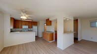 This two-story home is designed with a practical, open layout that promotes a bright and functional living environment. The main level centers around a spacious open-concept living and kitchen area, where light wood-style laminate flooring flows throughout. A ceiling fan overhead provides comfort, while natural light pours in through well-placed windows. The kitchen is well-appointed with warm-toned wood cabinetry, light countertops offering ample workspace, and white appliances including a range, over-the-range microwave, and refrigerator. A peninsula with a breakfast bar adds additional counter space and defines the transition between the kitchen and living area. A staircase with a decorative iron railing connects the main level to the upper floor. The bedrooms feature the same wood-style flooring, windows for natural light, and sliding or standard closets providing useful storage. The bathrooms are finished in a clean, neutral palette, each featuring wood-toned vanities, white countertops, and light flooring. One bathroom includes a tub-shower combination with a glass sliding door, while another features a standalone walk-in shower. Overall, the home presents a clean, functional interior with consistent finishes throughout both levels.