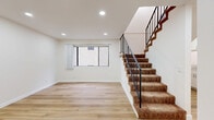 Located in North Hollywood, this two-story, 2-bedroom, 2-bathroom home offers a well-organized layout spread across two floors. The main level features a bright living room with light wood-style flooring, recessed lighting, and a carpeted staircase with a sleek black metal railing leading to the upper level. The combined kitchen and dining area is highlighted by warm wood flooring, a modern chandelier, a pass-through counter, and a wall-mounted AC unit. A sliding glass door opens onto a private balcony with views of the surrounding urban neighborhood. Both bedrooms are finished with plush carpet, ample closet space with sliding doors, and wall-mounted AC units, offering a comfortable and functional retreat. The primary bedroom is generously sized, providing room for versatile furnishing arrangements. The two bathrooms are finished with light wood flooring, white cabinetry with brushed nickel hardware, and stone-look countertops. One bathroom includes a tub and shower combo with a sliding glass door. Clean white walls and consistent finishes throughout give the home a cohesive, modern feel well-suited for everyday living in Los Angeles.