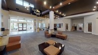 The Club Palisades Apartments amenity and leasing center at 2211 S Star Lake Road in Federal Way, Washington, offers a well-appointed, single-floor facility designed to serve residents with both functional and social spaces. The grand lobby greets visitors with soaring ceilings, exposed dark wood beam accents, and a latticed wood ceiling detail that adds warmth and architectural character. Large windows along the entrance flood the space with natural light, while recessed and track lighting provide consistent illumination throughout.

The central lobby features comfortable seating arrangements with modern upholstered chairs and ottomans, creating an inviting gathering space. A dedicated leasing area showcases a glass-top consultation desk set against a striking stacked stone accent wall, adorned with framed artwork. An adjacent lounge nook, also wrapped in stacked stone, offers plush leather seating for a more intimate setting.

A well-equipped business center provides multiple workstations with computers and individual task lighting, complemented by colorful wall art. The fitness center is generously sized, outfitted with treadmills, ellipticals, cable machines, and free weights, with large mirrors and windows enhancing the sense of openness. Throughout the facility, neutral-toned carpet, light wood flooring, and curated artwork contribute to a cohesive, upscale aesthetic.