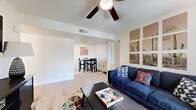 Located at 125 S Dobson Rd in Chandler, Arizona, this single-floor residence offers three bedrooms, two bathrooms, and three dedicated closets within a well-organized layout. The open-concept living, dining, and kitchen area forms the heart of the home, finished with light wood-style flooring and a textured ceiling. The living room features a ceiling fan, a wall-mounted TV setup, and a window that allows natural light to fill the space. A gallery-style arrangement of desert-themed wall art adds a nod to the Arizona surroundings. The galley kitchen is equipped with white cabinetry, white countertops, a double stainless steel sink, and a full suite of appliances, maximizing efficiency in a compact footprint. The primary bedroom provides a comfortable retreat with a ceiling fan, natural light from a window with vertical blinds, and direct access through double doors to a walk-through closet leading to a private bathroom with a vanity and sink. The additional bedrooms each include ceiling fans, windows, and dedicated closets. The two bathrooms are clean and functional — one featuring a full tub-shower combination with a curved curtain rod, and the other a straightforward vanity and toilet configuration. Light wood flooring runs consistently throughout the residence, creating a cohesive and bright atmosphere.
