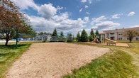 Located at 9123 Cleveland St in Merrillville, Indiana, this well-appointed outdoor recreational space offers a variety of amenities designed for active community living. The grounds are thoughtfully landscaped with a mix of mature evergreen and deciduous trees, including blue spruce and multi-stem ornamentals, providing natural shade and visual interest throughout the property.

A dedicated children's playground sits at the heart of the space, featuring a multi-level play structure with slides, climbing elements, and tunnels, all set atop a generous wood chip safety surface enclosed by border edging. Adjacent to the playground, a full-size sand volleyball court invites residents to enjoy friendly competition, set within a well-maintained sandy surface framed by green lawn.

Open stretches of manicured grass provide ample room for informal recreation and gatherings. Picnic seating is available near the playground area, and posted playground rules signage reflects a commitment to safe, community-friendly use of the space. The grounds border a multi-story residential building with balconies that overlook the outdoor area, reinforcing the community-oriented character of the property. A pergola or covered structure is also visible near the volleyball area, adding a shaded retreat option. Overall, the space presents a clean, inviting, and active outdoor environment suited for residents of all ages.