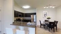 Located at 1150 Helen Drive in Newark, Delaware, this single-floor residence offers a thoughtfully designed living environment with modern finishes and an open, airy layout. The kitchen is a standout feature, showcasing rich dark cabinetry that extends to the ceiling, providing ample storage alongside a sleek granite countertop with bold veining. A peninsula with bar seating serves as both a functional workspace and a casual dining spot, seamlessly connecting the kitchen to the rest of the living area. Stainless steel appliances, including a refrigerator, microwave, and range, lend a contemporary, polished look to the space. The kitchen flows naturally into a dedicated dining area, which comfortably accommodates a full dining table and chairs, making it well-suited for both everyday meals and entertaining. Neutral-toned flooring and walls throughout create a bright, welcoming ambiance, complemented by recessed and flush-mount lighting that ensures the space is well-lit. The overall design balances practicality with style, offering a cohesive and functional living environment ideal for modern living.